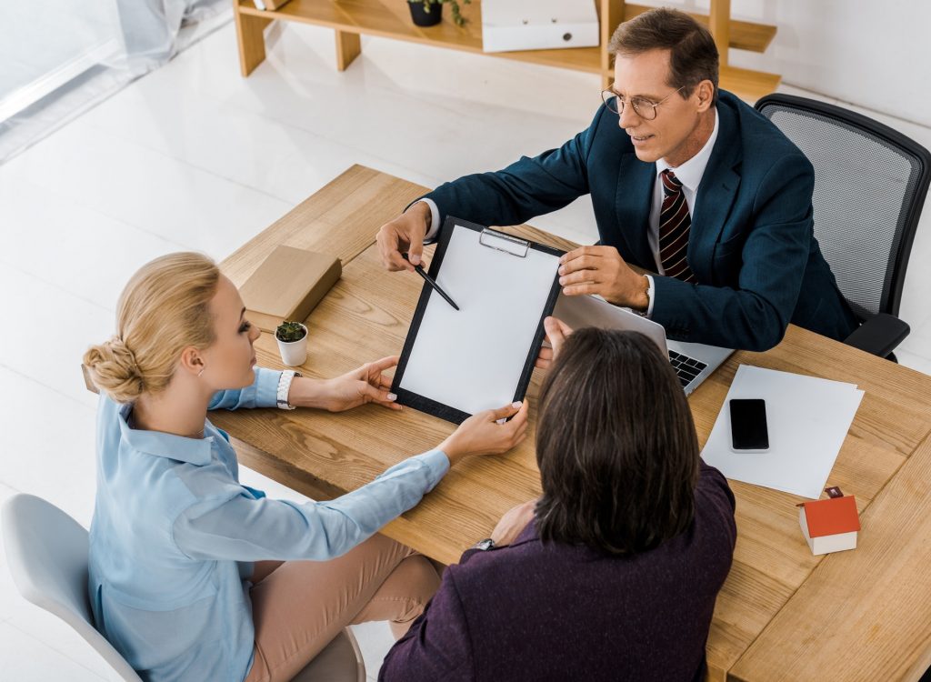 adult insurance agent in glasses showing contract to young couple in office